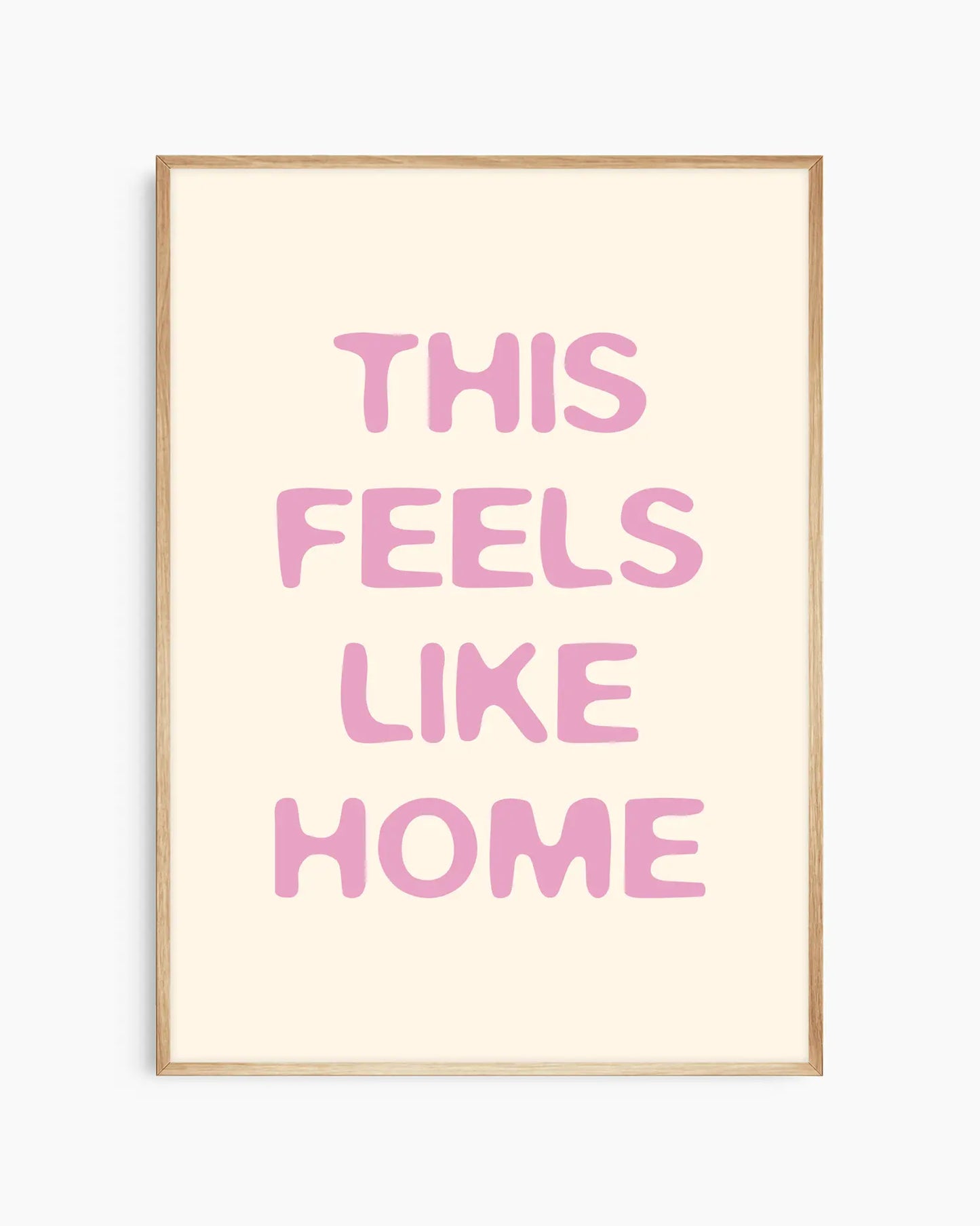 Nursery poster with the text 'This feels like home' written in pink on a beige background, framed in an oak frame