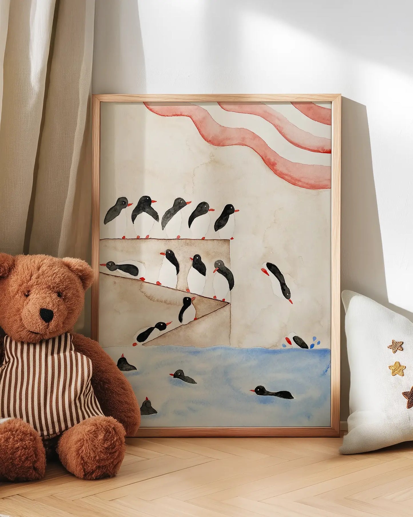 Framed artwork with penguins on a wall next to a teddy bear and decorative pillow.
