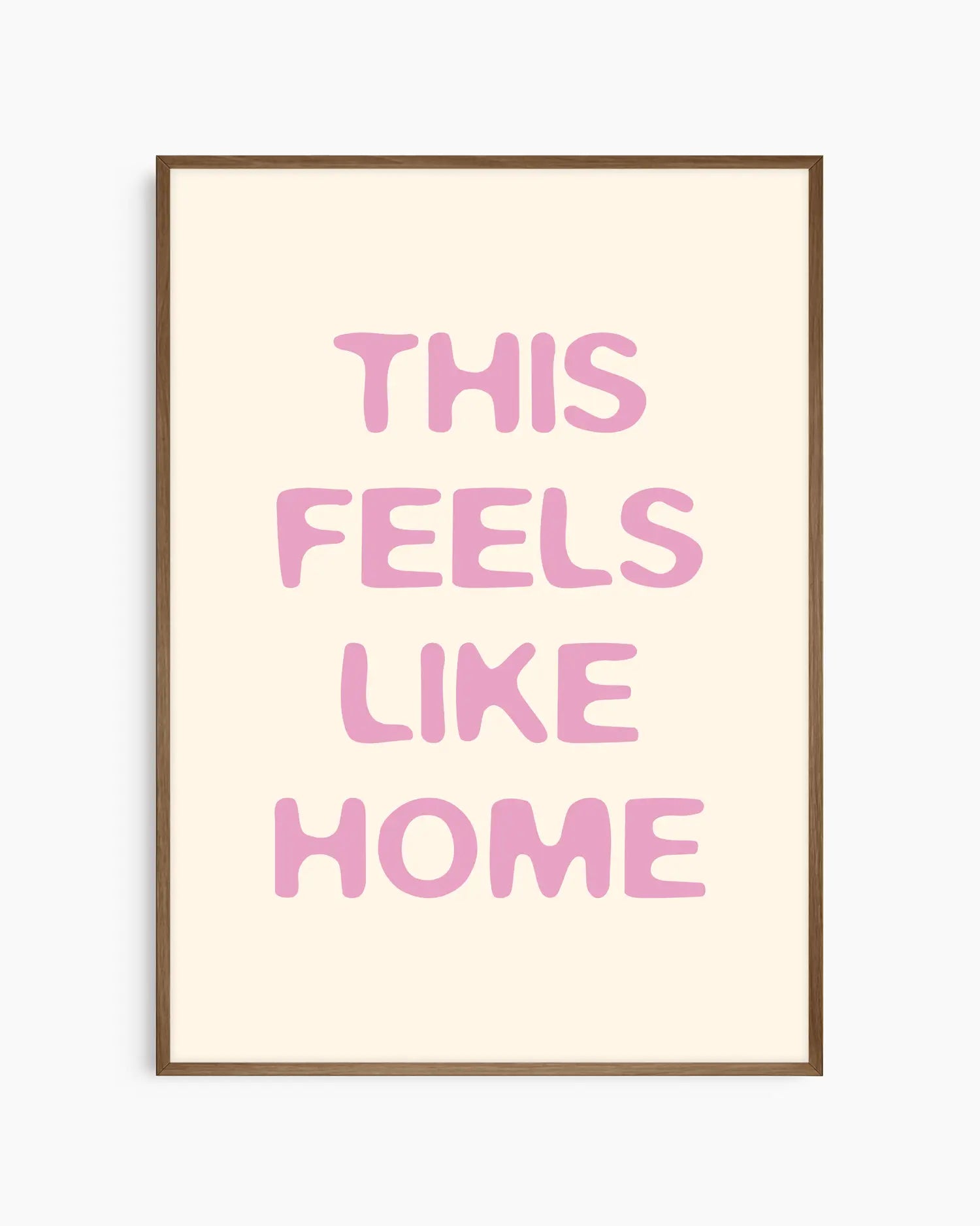 Nursery poster with the text 'This feels like home' written in pink on a beige background, framed in a dark oak frame